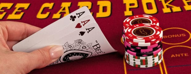 Close-up of a player holding three aces in Three Card Poker with stacks of chips on the table at California Grand Casino