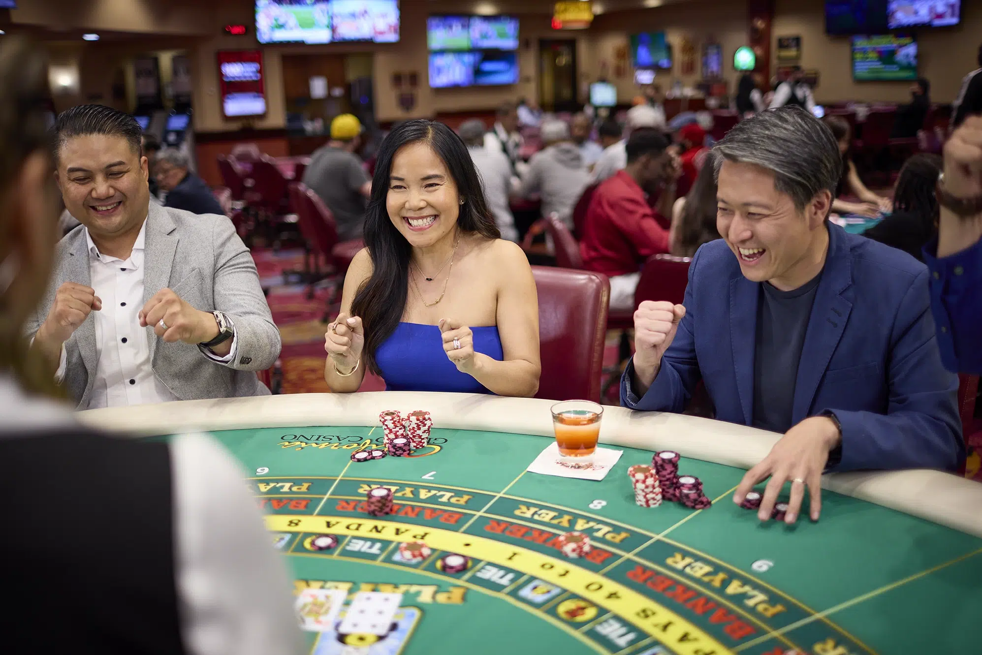 Group of players cheering at an EZ Baccarat table with chips and playing cards in a casino